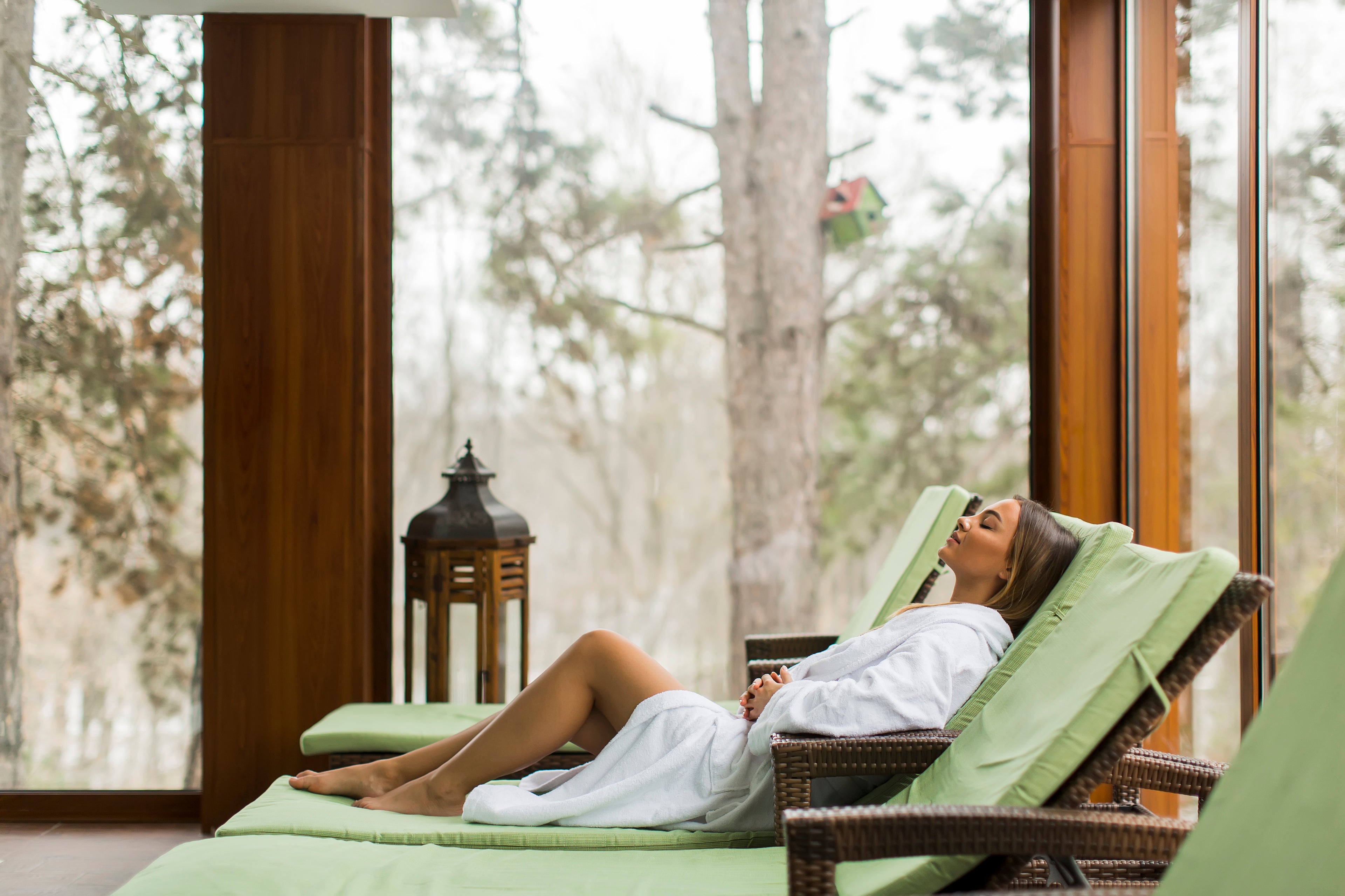 Woman in a white robe lying on a green lounge chair with a scenic view outside.